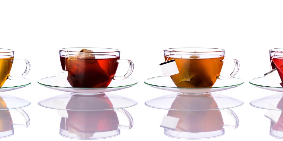 Vier Teegläser sind mit unterschiedlichen Teesorten gefüllt vor einem weißen Hintergrund.