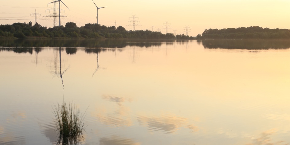 Ein See bei Sonnenuntergang im Hintergrund Windräder.