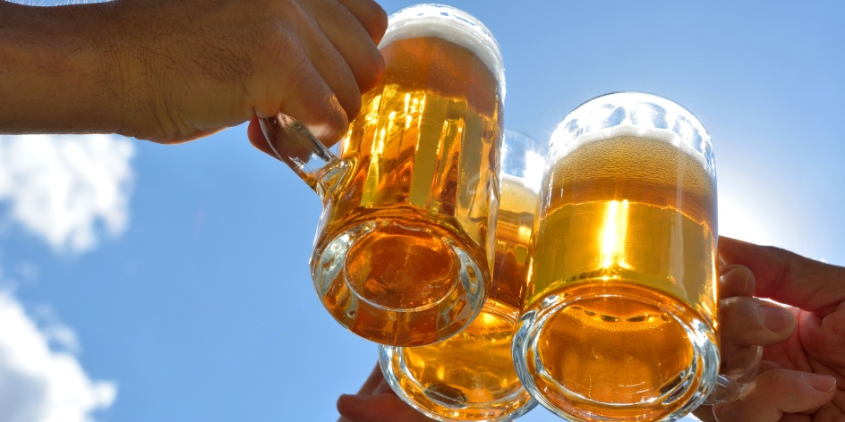 Es sind drei Hände die Biergläser halten und vor blauem Himmel miteinander anstoßen.