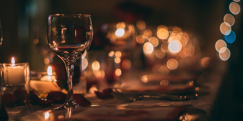Ein romantisch eingedeckter Tisch mit polierten Gläsern, Kerzenschein und Rosenblättern