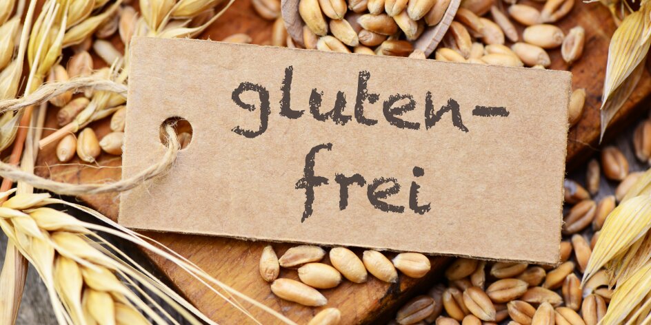 Zu sehen ist ein Schild mit der Aufschrift "Glutenfrei". Im Hintergrund sind Weizenkörner zu sehen. 