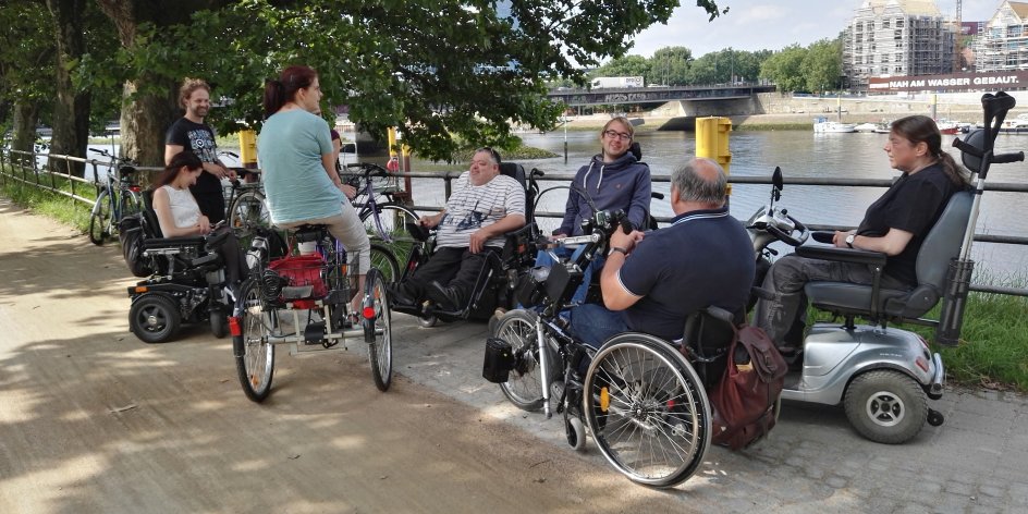 Eine Gruppe von Menschen in Rollstühlen, mit Handbike und Dreirad an der Weser.