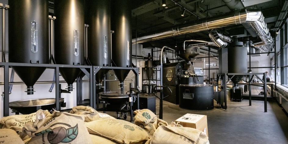Blick in die Azul Rösterei am Deich mit Kaffeesäcken im Vordergrund, im Hintergrund Geräte für den Röstvorgang