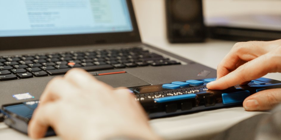 Ein Laptop mit Braillezeile, Hände ertasten den Text in Blindenschrift.