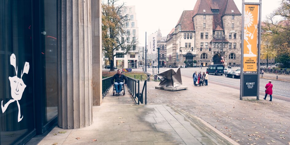 Ein Mann im Rollstuhl fährt die Rampe vor der Kunsthalle Bremen herauf.