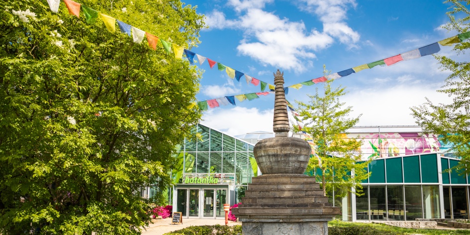 Ein buddhistisches Monument (Stupa), an dem Gebetsfahnen hängen, steht vor der botanika.