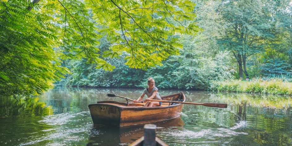 Eine Frau fährt mit einem Ruderboot durch ein Waldstück