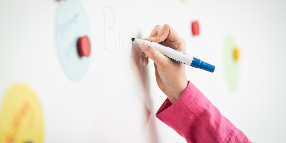 Eine Frauenhand schreibt auf ein Whiteboard das Wort Bildung