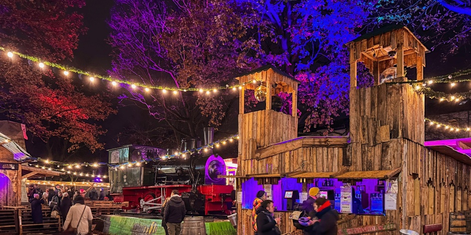 Beim Findorffer Winterdorf stehen rund um die Jan-Reiners-Lok Buden aus Holz, an denen Menschen bei weihnachtlicher Beleuchtung zusammenkommen