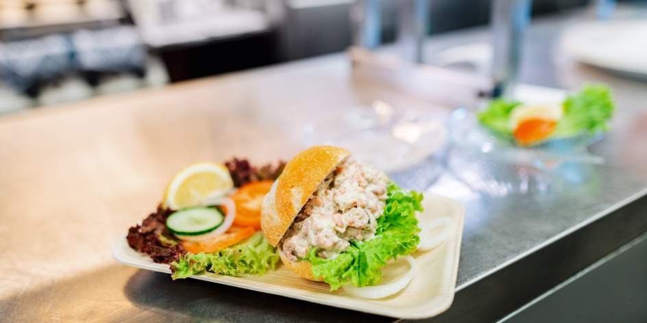 Ein Krabbenbrötchen garniert mit Salat auf einem Teller.