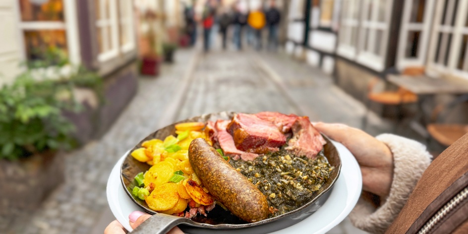 Eine Person hält eine Grünkohlpfanne im Schnoor in die Luft.