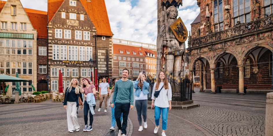 Eine Gruppe jüngerer Menschen besichtigt den Bremer Marktplatz mit Rathaus und Roland