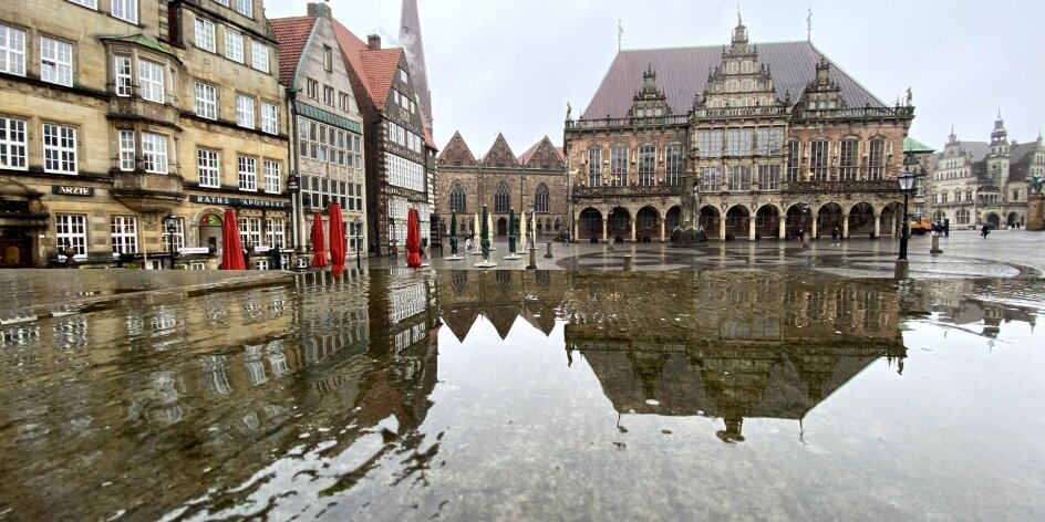 Historische Gebäude spiegeln sich auf einer nassen Fläche.