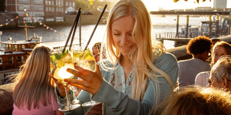 Eine Frau hält mehrere Cocktailgläser an der Hand. 