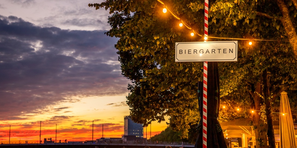 Ein Schild auf dem "Biergarten" steht. Im Hintergrund ist die Weser zu sehen, während die Sonne untergeht.