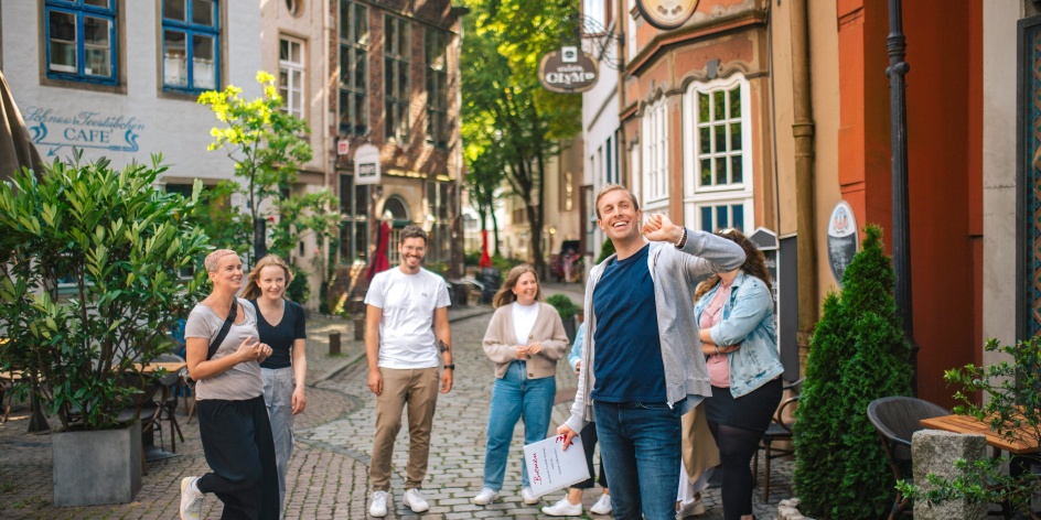 Ein Mann führt eine Gruppe durch das Schnoorviertel vorbei an kleinen Häusern in einer schmalen Gasse.