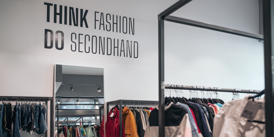 A second-hand store with lots of clothes rails. “Think Fashion Do Secondhand” is written in thick black letters on the wall