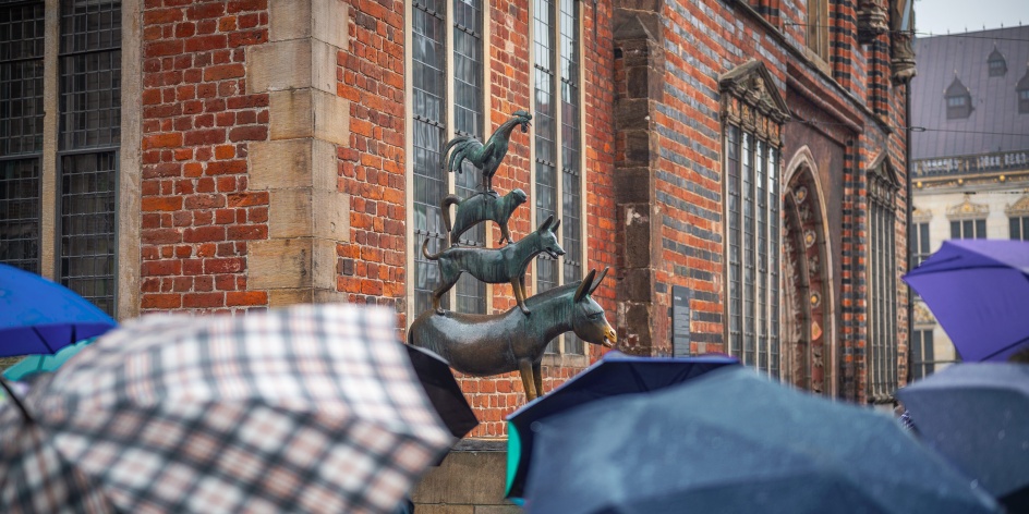 Die Statue der Bremer Stadtmusikanten ist umringt von Menschen mit Regenschirmen.