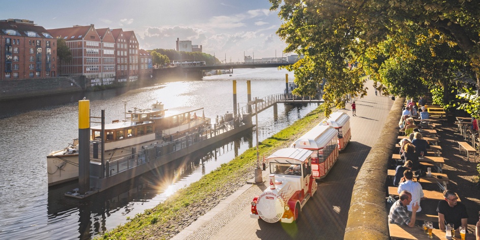 Eine kleine Bummelbahn fährt an einer Promenade entlang.