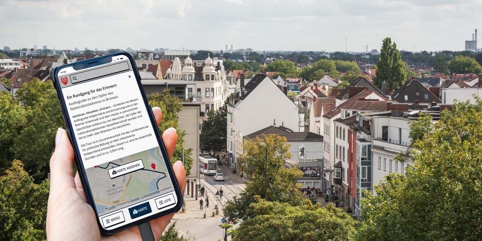 Hand hält Smartphone mit Audioguide-App über einer Stadtansicht mit Häusern, Straßen und viel Grün.