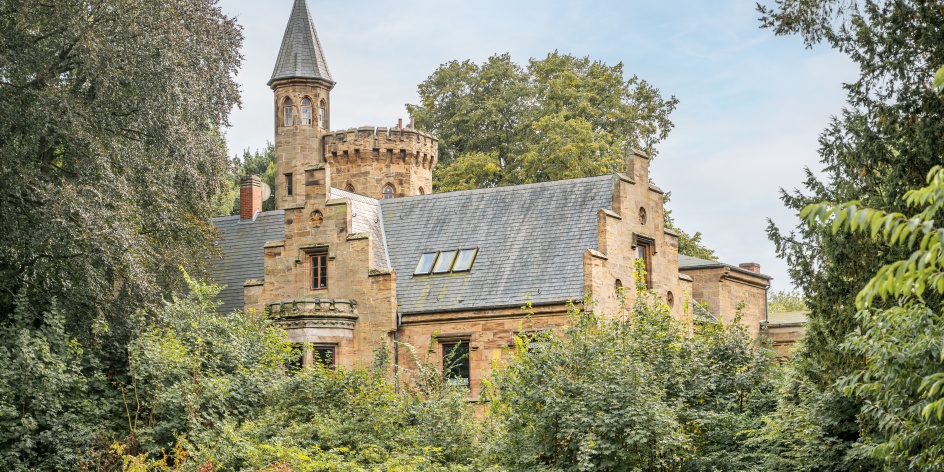 Das Wätjens-Schloss vom Weiten und eingebettet von Bäumen und Büschen.