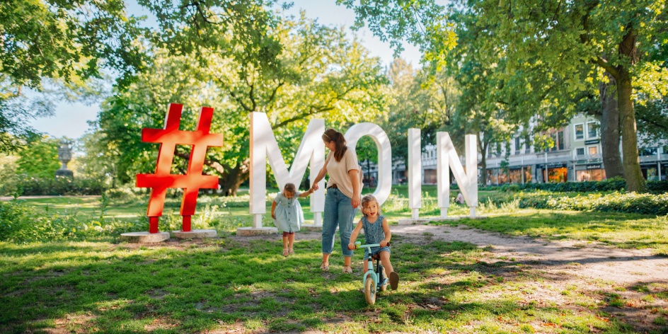 Das Foto zeigt eine Mutter mit ihren Kindern vor den Moin-Buchstaben in Bremen.