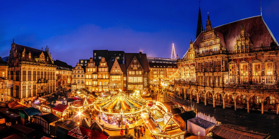 Eine historische Kulisse mit einem Weihnachtsmarkt, der in der Abendstimmung leuchtet.