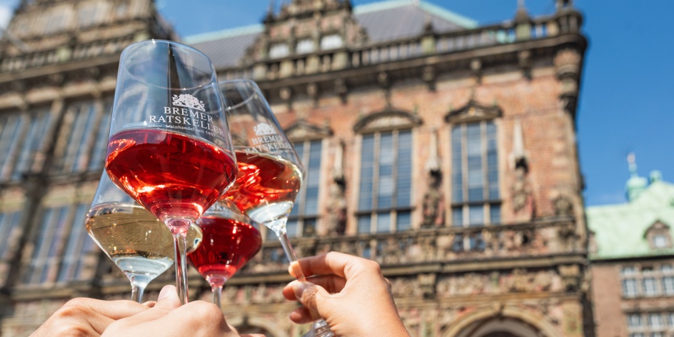 Vier Personen stoßen mit einem Weinglas vor dem Bremer Rathaus an.