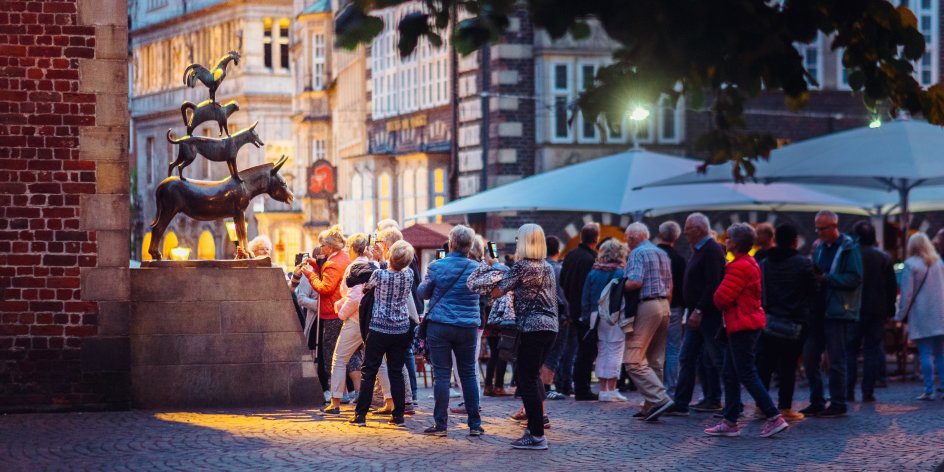 Die Aufnahme zeigt viele Menschen, die am Abend vor der Bronzestatue der Bremer Stadtmusikanten stehen und Bilder machen. 
