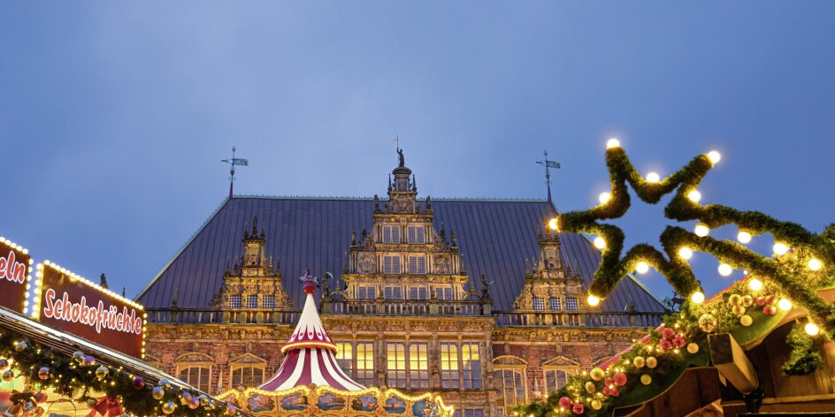 Vor der historischen Kulisse des Bremer Rathauses funkeln weihnachtlich beleuchtete Verkaufsstände und Karussells