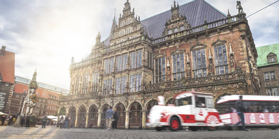 Eine Art kleine Bimmelbahn fährt vor dem historischen Rathaus in Bremen entlang.