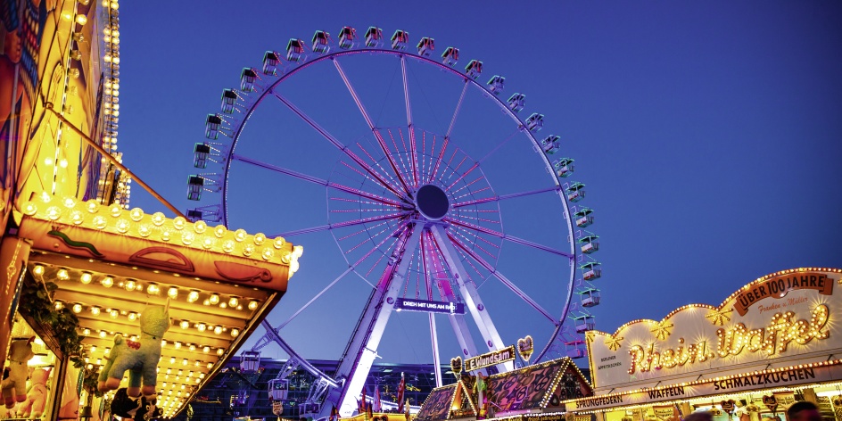 Die Osterwiese am Abend. Menschen schlendern an den Buden vorbei. Im Hintergrund leuchtet ein Riesenrad