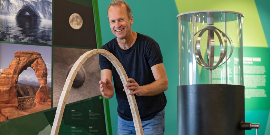 Ein Mann der vor einer grün-gelben Wand steht und ein Experiment demonstriert.