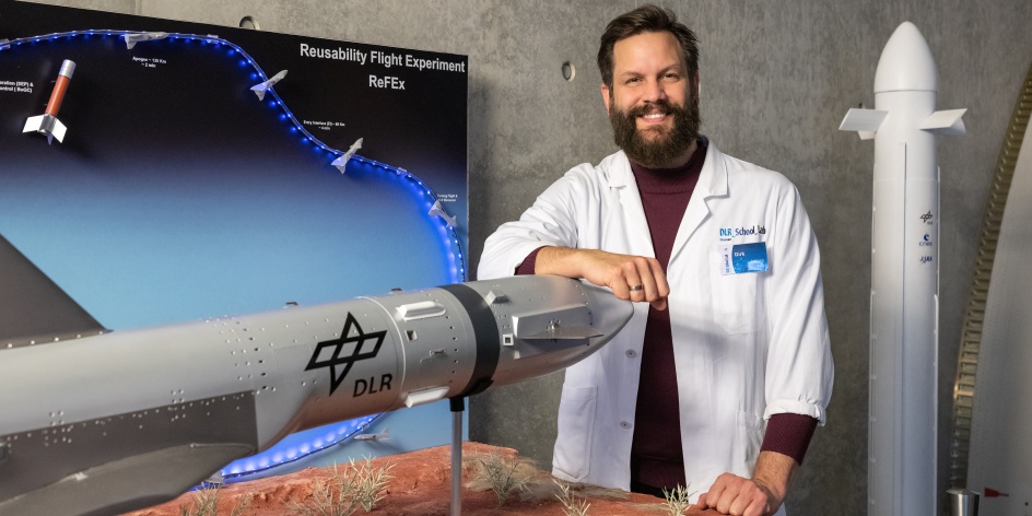 Ein Mann, der hinter einem Modell einer Rakete steht, auf der "DLR" geschrieben steht.