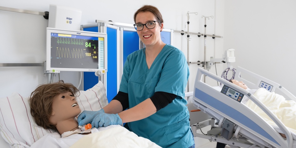 Eine Frau in medizinischer Kleidung demonstriert eine Behandlung an einer Puppe.
