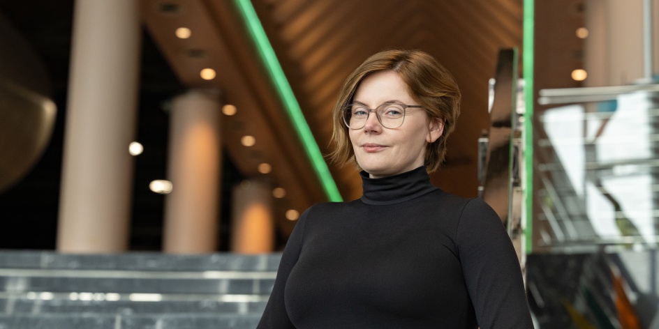 Eine Frau steht in eleganter, schwarzer Kleidung vor einer Treppe.