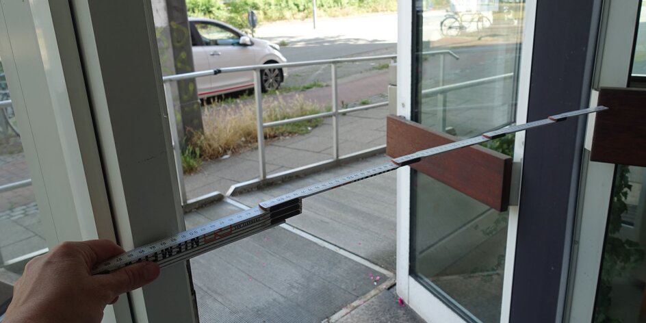 Die Breite einer Eingangstür wird mit einem Zollstock vermessen.