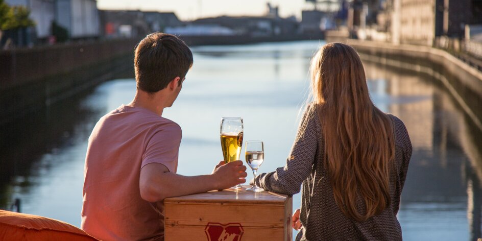 A couple sits in the evening sun on the terrace of the Feuerwache in Überseestadt and looks out over the harbour basin.