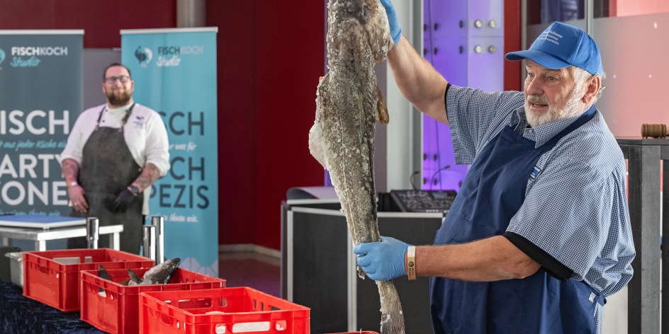 Ein Mann hält einen großen Fisch in die Höhe und präsentiert ihn.