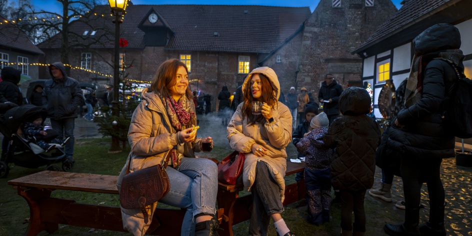 Zwei Frauen sitzen mit einem Glühwein an einer Feuerstelle.
