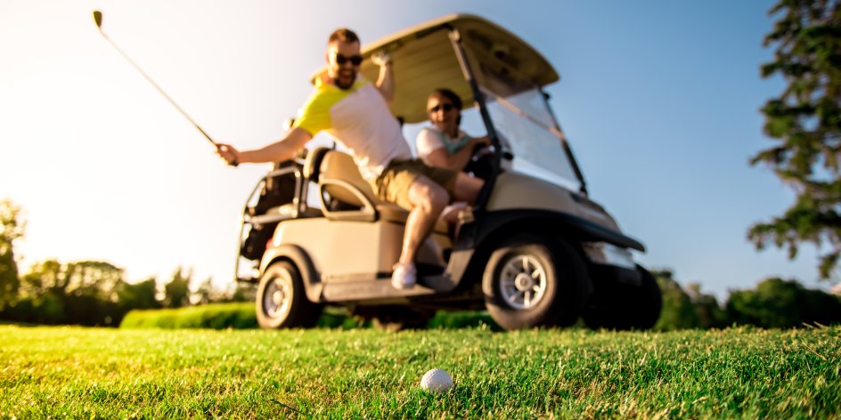 Zwei Männer sitzen in einem Golfcart und schlagen einen Ball. 