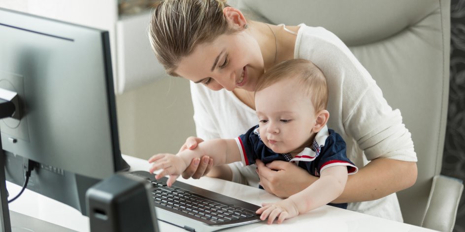 Eine lächelnde Frau sitzt mit einem Kleinkind am Computer.