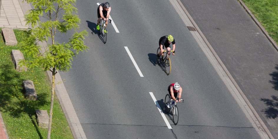 Triathlon-Teilnehmer fahren auf Fahrrädern über die Straße.