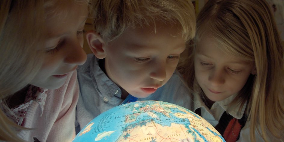 Drei Schüler betrachten einen leuchtenden Globus