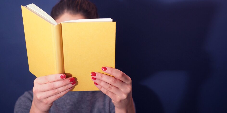 Eine Frau hält ein Buch vor ihr Gesicht.