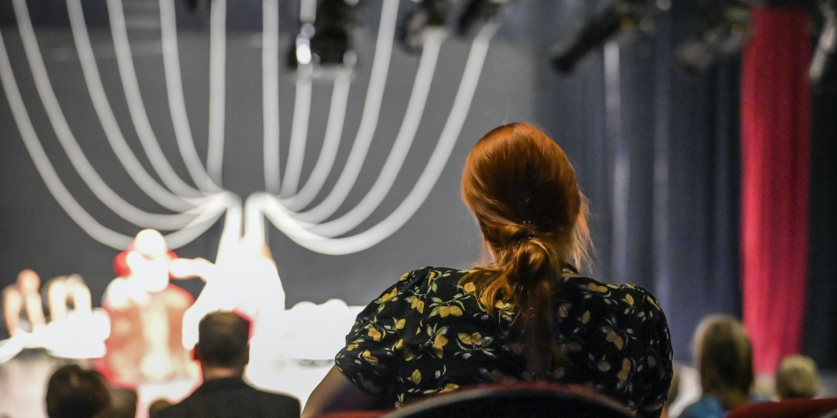 Eine Frau sitzt im Publikum und schaut einer Bühnenshow zu.