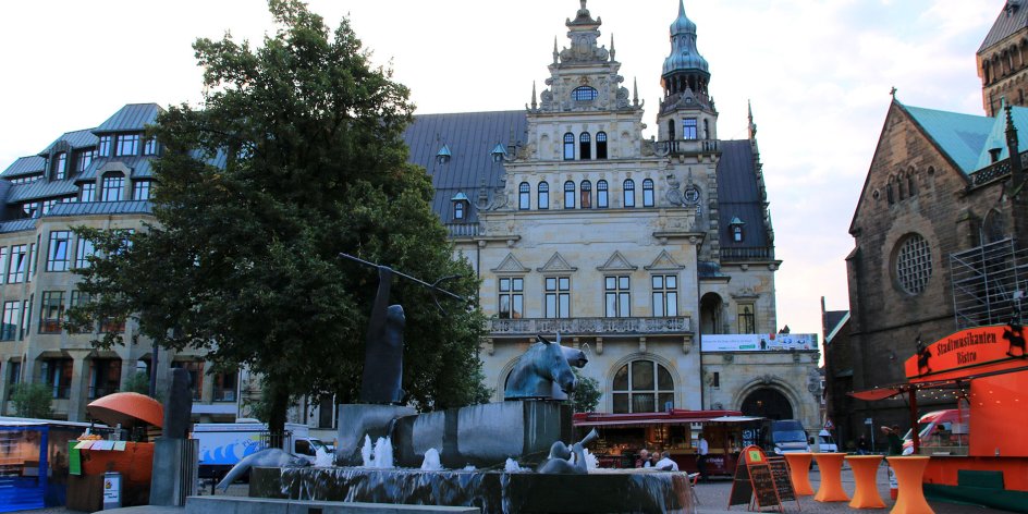 Im Hintergrund liegt das historische Gebäude der Bremer Bank. Davor reihen sich einige Marktstände sowie der Neptunbrunnen am Marktplatz.