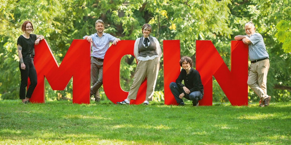 Die fünf Local Heroes der Kampagne Erlebe das Moin stehen an den Moin-Lettern in den Wallanlagen