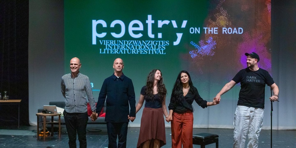 Fünf Personen stehen auf einer Bühne und halten sich an den Händen. Im Hintergrund wird das Logo von poetry on the road an die Wand geworfen.