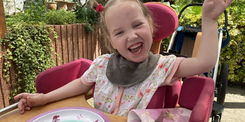 Ein lachendes Mädchen am Esstisch im Garten. 